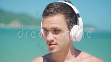 拥抱英俊的年轻人，用无线白耳机听他的智能<strong>手机音乐</strong>，在海滩上跳舞。